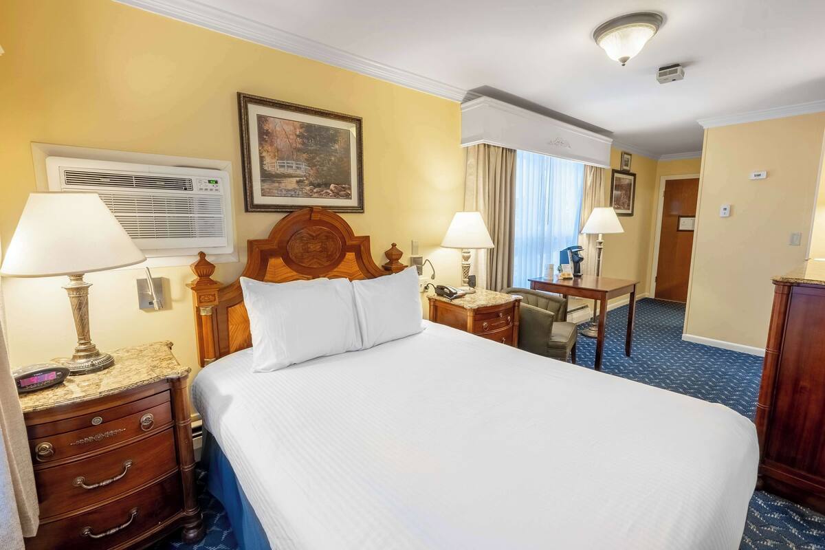 A hotel room with a large bed, two bedside tables with lamps, a desk, a chair, and a painting on the wall.
