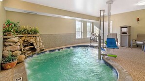 An indoor swimming pool with a stone wall and plants, a blue slide, and a seating area with chairs.