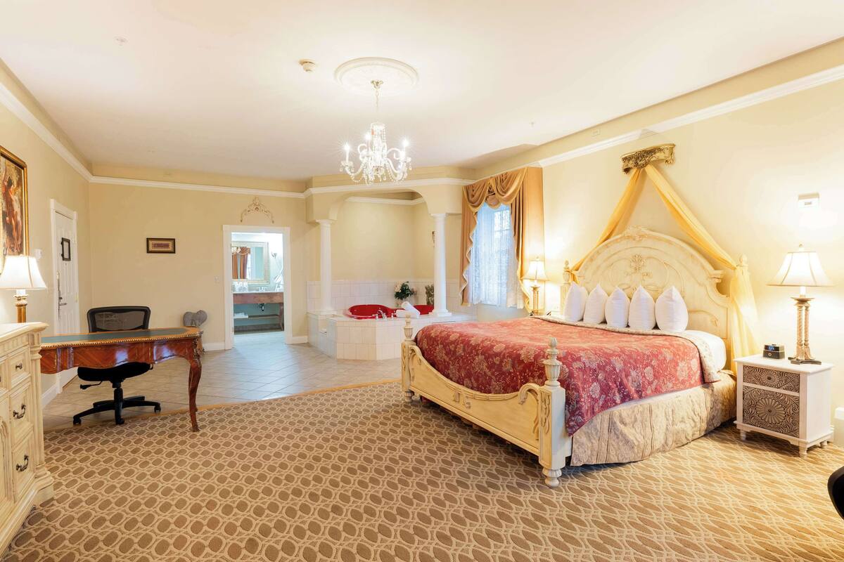 A spacious bedroom with a large bed, a desk, and a separate bathroom area.