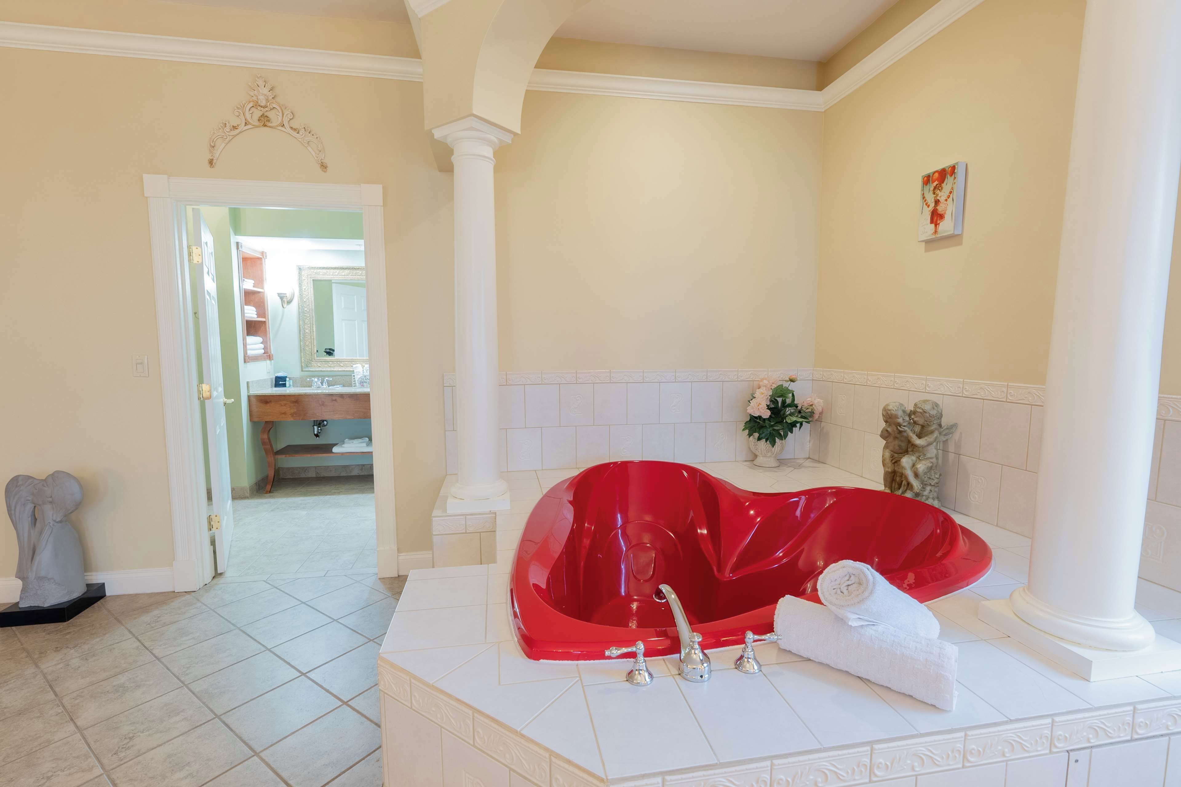 Un baño con una bañera roja, columnas blancas y un lavabo blanco.
