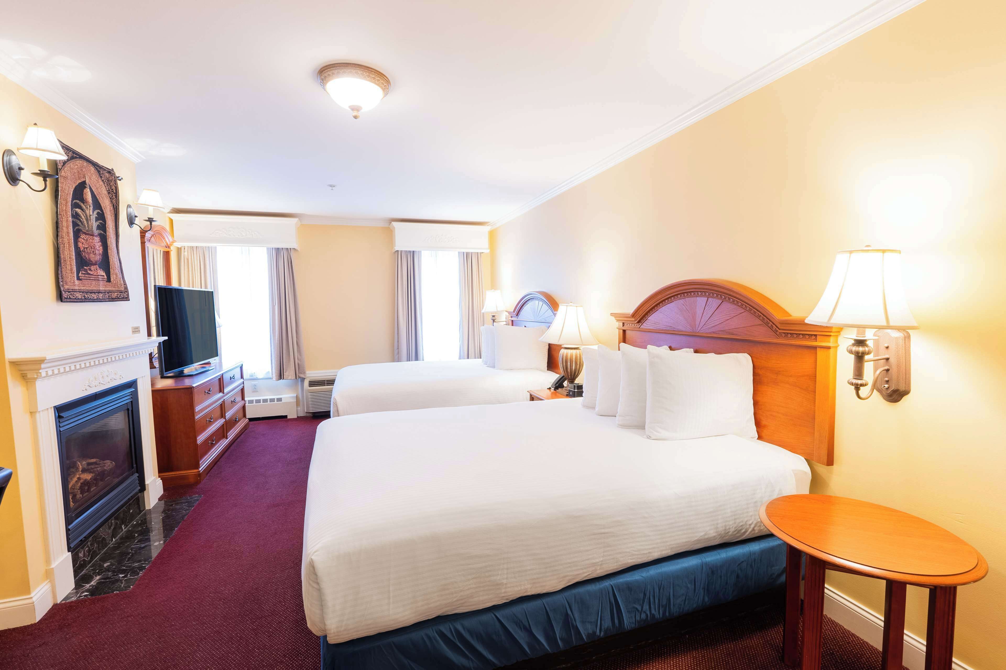A hotel room with two beds, a fireplace, a television, and a small table.