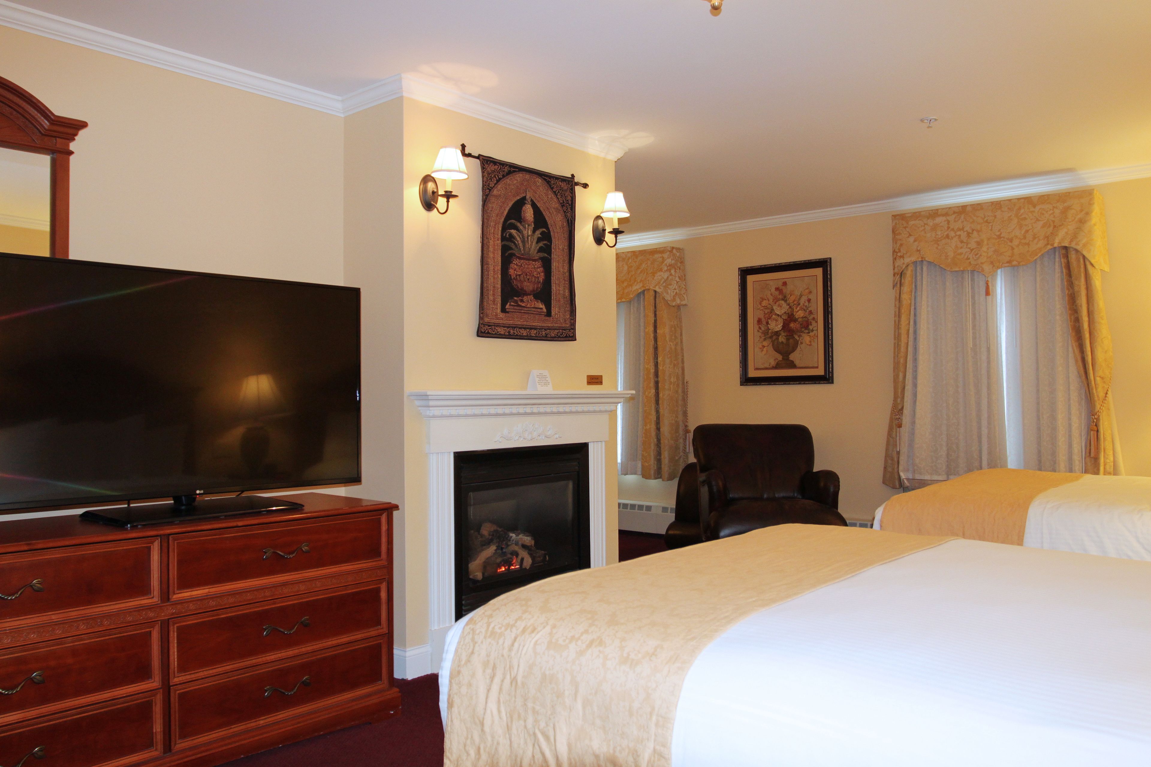 A hotel room with a flat-screen TV, a fireplace, two beds, a chair, and wall-mounted lamps.