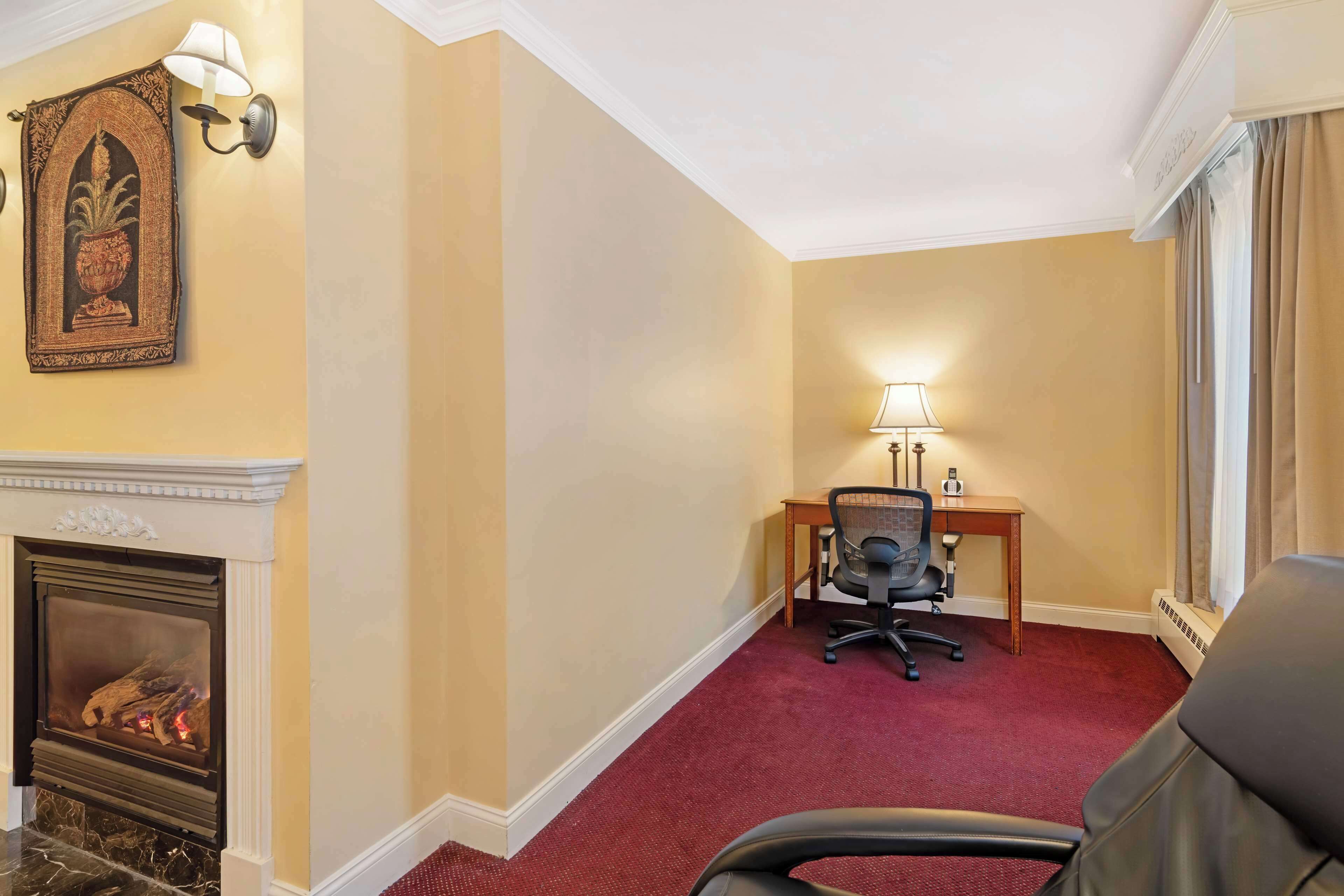 Une chambre d’hôtel avec une cheminée, un bureau avec une chaise et une lampe.