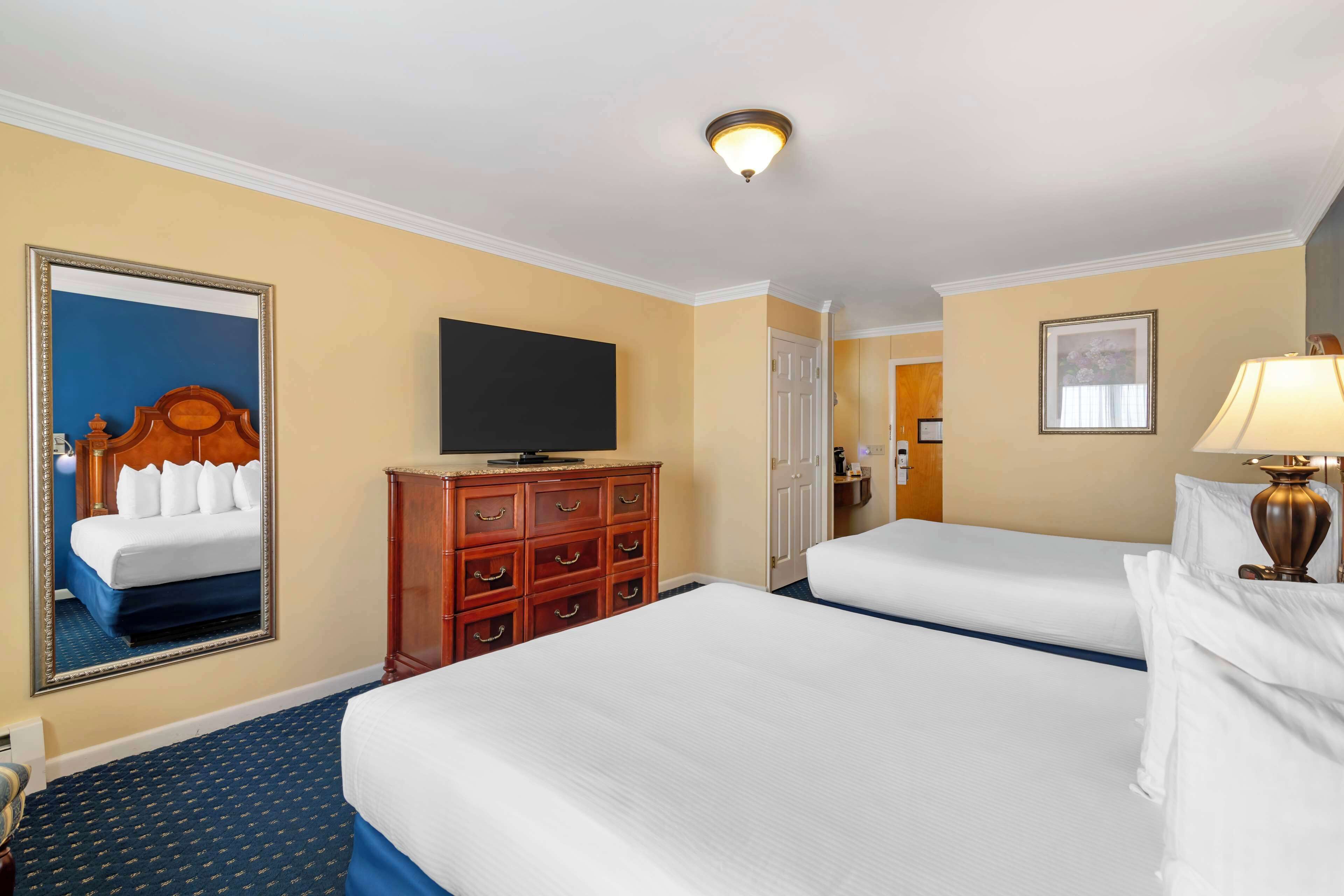 A hotel room with two beds, a dresser, a television, and a mirror.