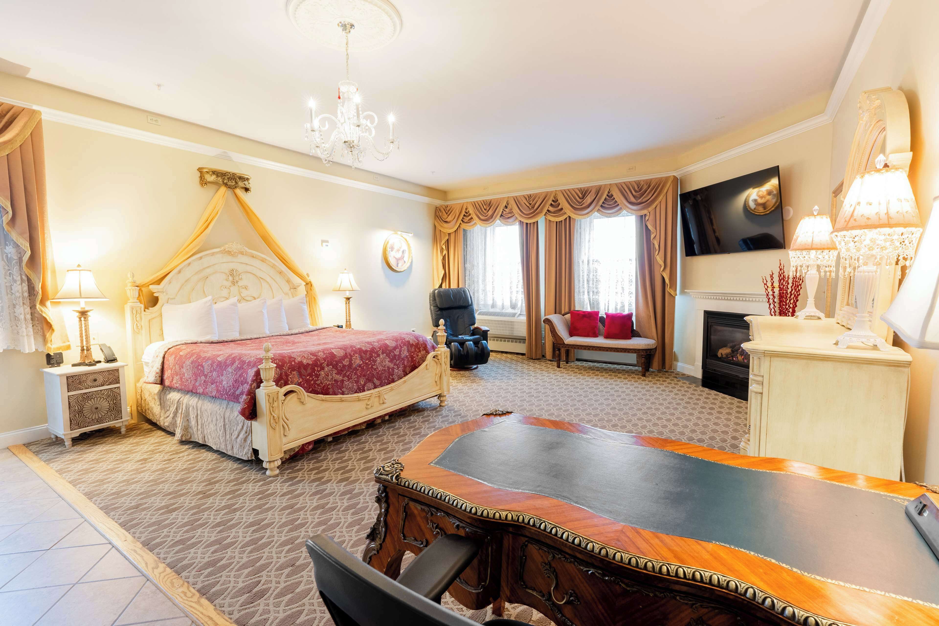 Een hotelkamer met een groot bed, een bureau, een stoel, een televisie en een open haard.