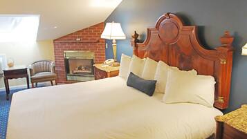 A hotel room with a large bed, a wooden headboard, a fireplace, a desk with a lamp, and a chair.