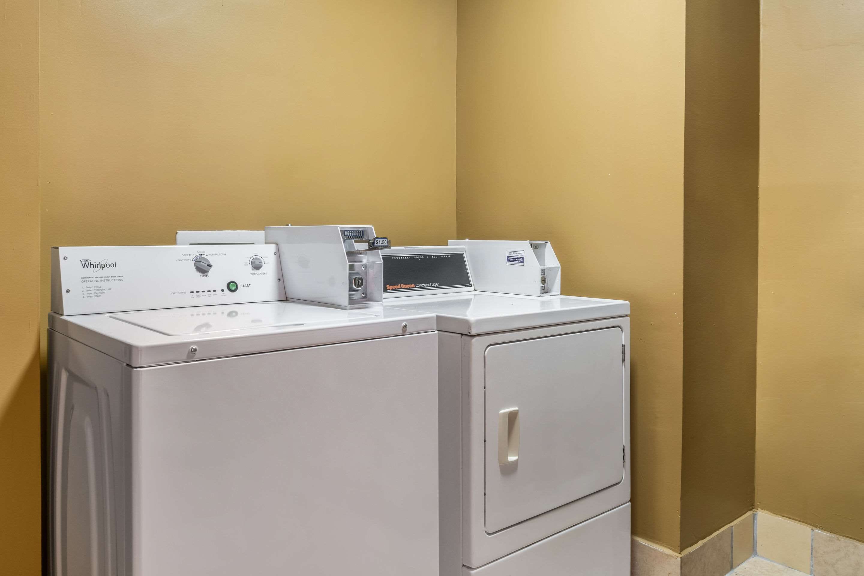 Un lave-linge et un sèche-linge Whirlpool à chargement frontal, installés dans une buanderie aux murs de couleur beige.