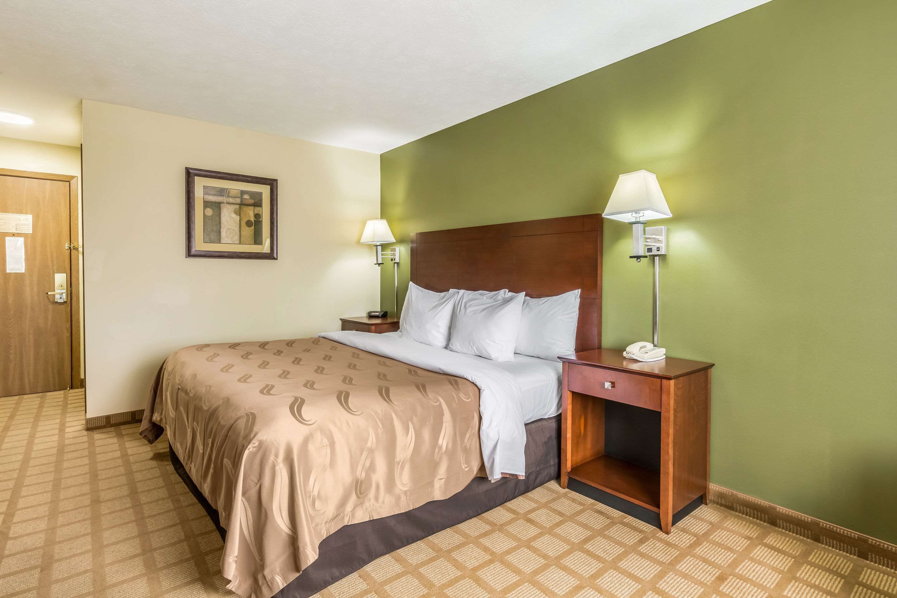 Habitación de hotel con una cama, dos lámparas de noche, una mesita de noche y un cabecero de madera.