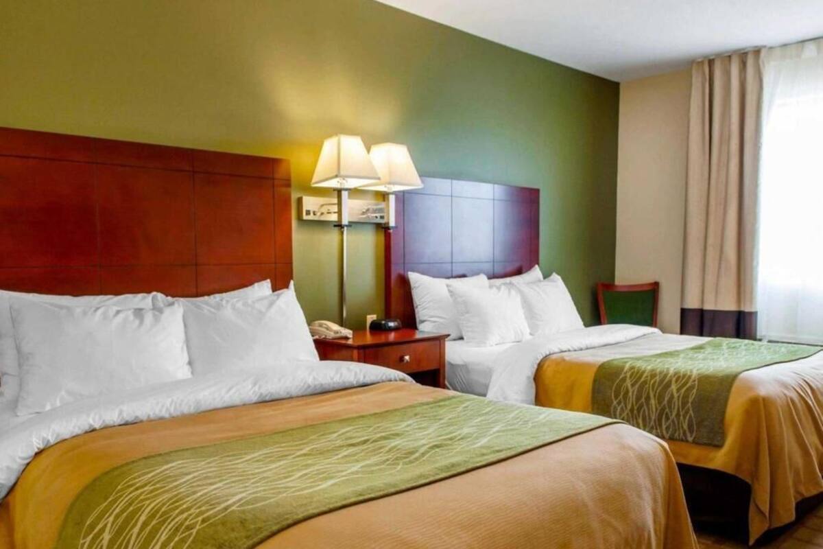 A hotel room with two beds, a nightstand with a lamp, a chair, and a window with curtains.