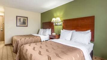 Una habitación de hotel con dos camas, una mesita de noche, una lámpara y un cuadro en la pared.