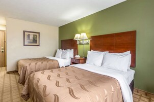Una habitación de hotel con dos camas, una mesita de noche, una lámpara y un cuadro en la pared.