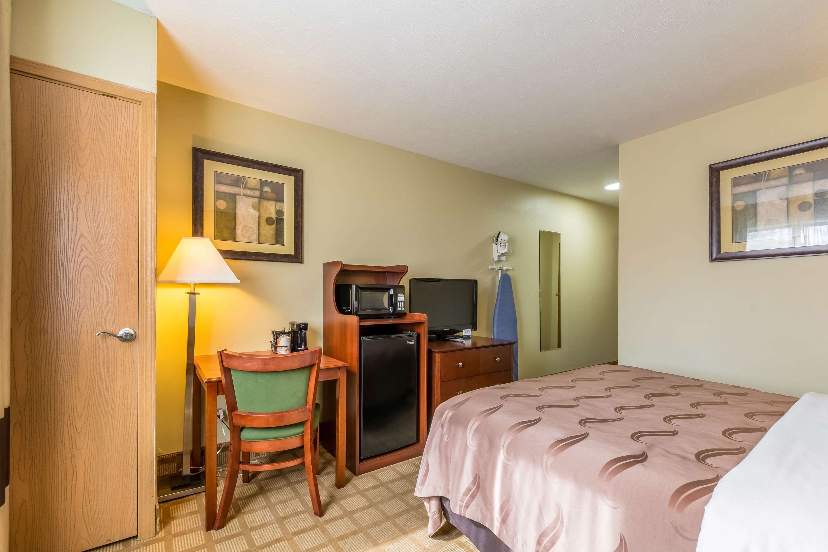 Une chambre d’hôtel comprenant un lit, un bureau avec une chaise, un four à micro-ondes, une télévision et une porte.