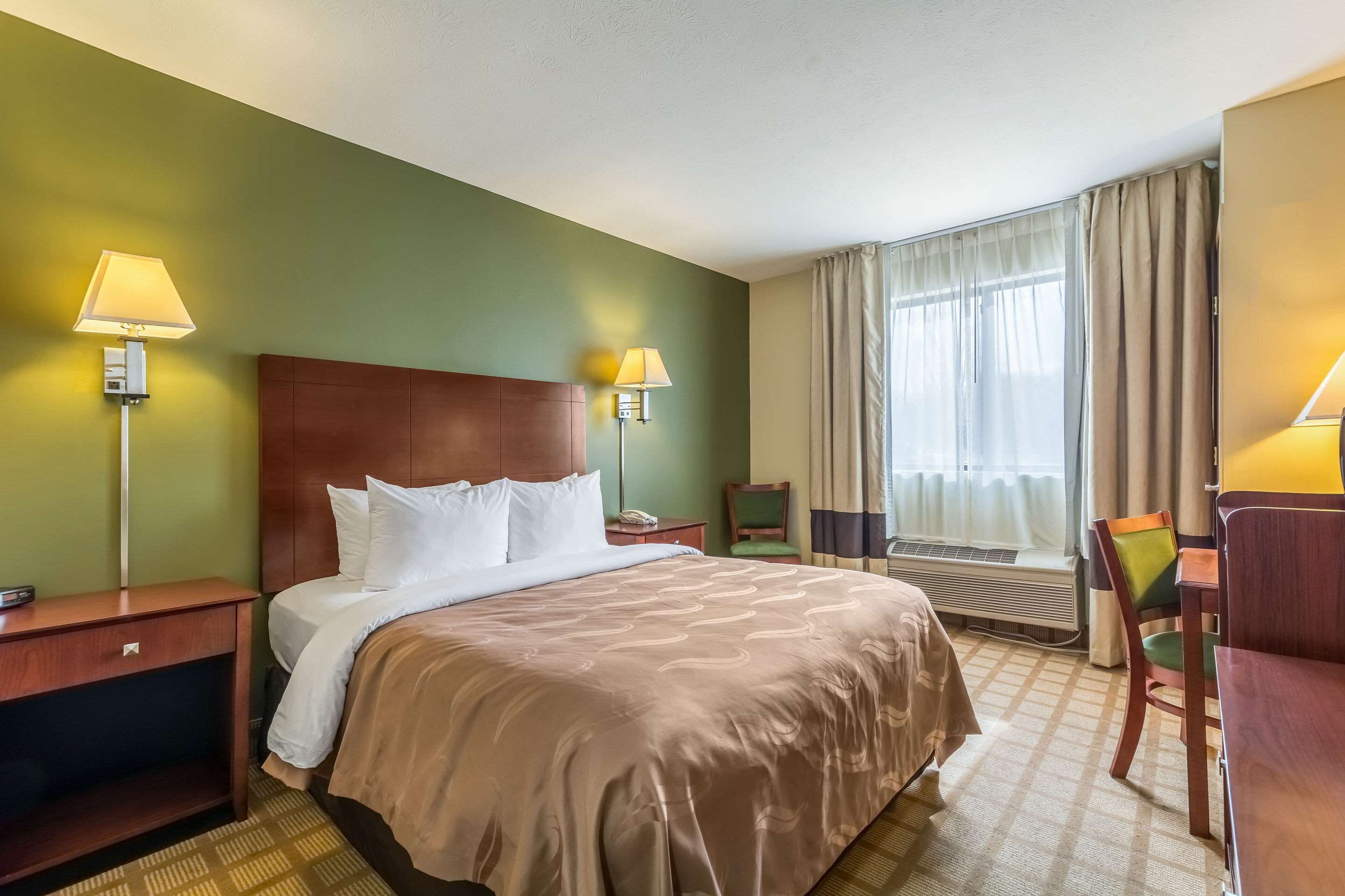 Habitación de hotel con una cama grande, dos lámparas de noche, un escritorio, una silla y una ventana con cortinas.