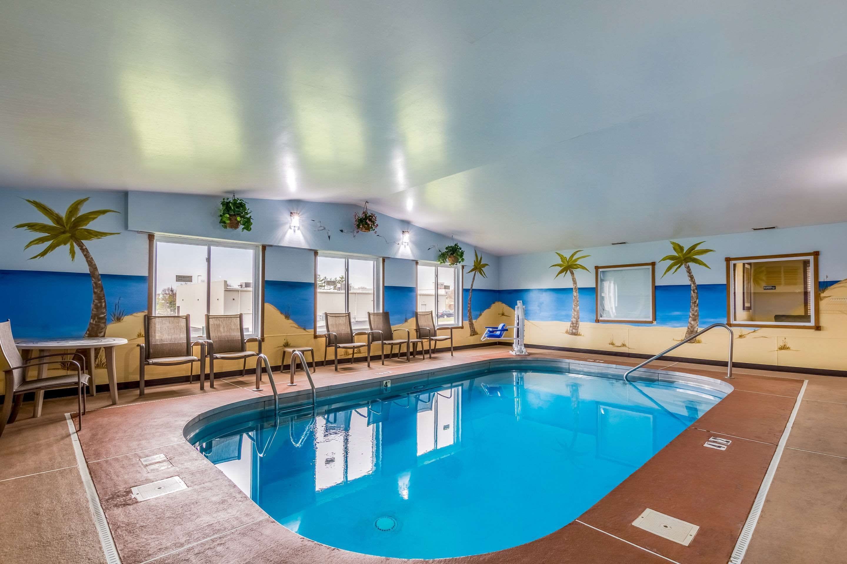 Una piscina interior con agua cristalina y azul, rodeada de sillones de descanso y una pequeña mesa.