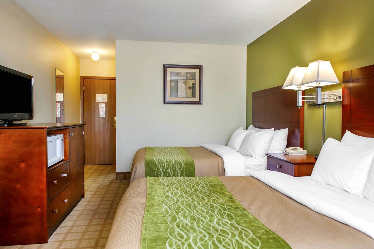 A hotel room with two beds, a television, a desk, and a lamp.