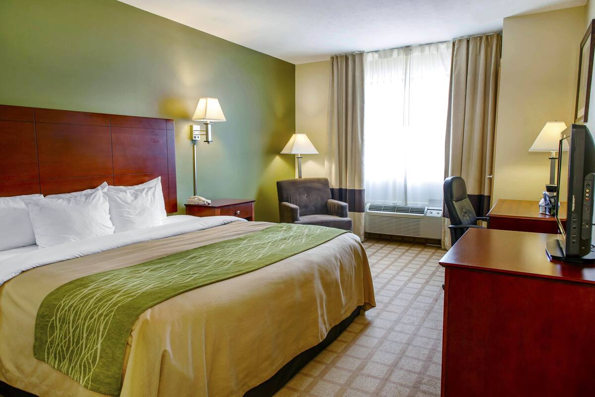 A hotel room with a large bed, two chairs, a desk with a computer, and a window with curtains.