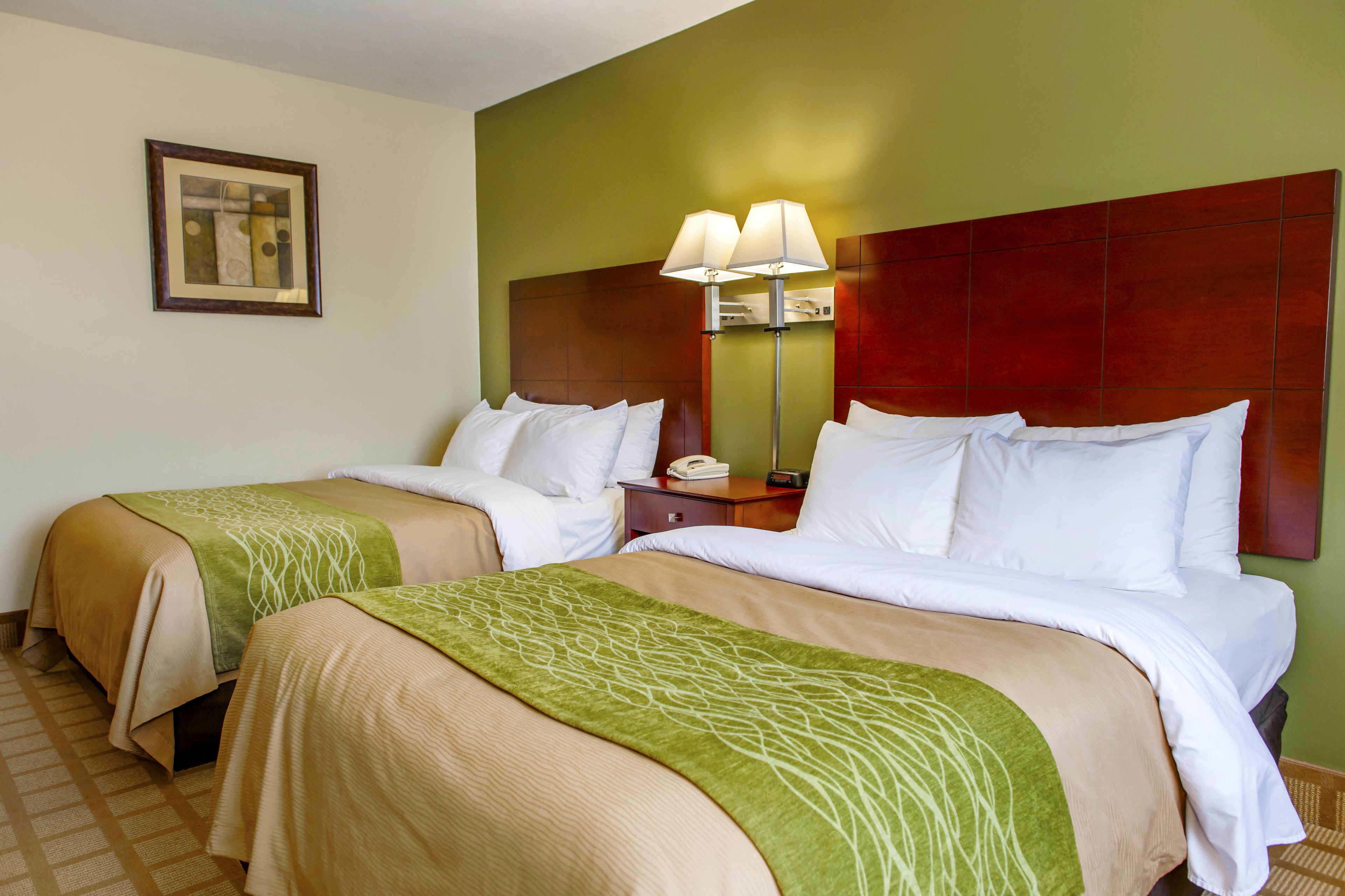 A hotel room with two beds, a nightstand, a lamp, and a framed picture on the wall.