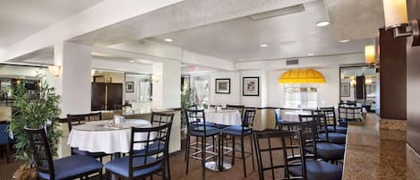 A spacious dining area with multiple tables and chairs, a central yellow umbrella, and a modern interior design.