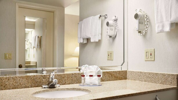 Une salle de bain d’hôtel avec un lavabo doté d’un plan de travail en granit, un miroir, un sèche-cheveux et des serviettes rangées sur un porte-serviettes.