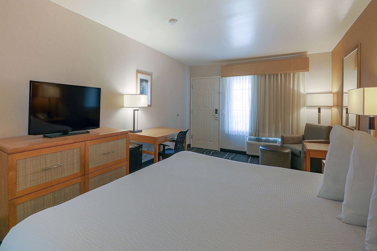 Ein Hotelzimmer mit einem großen Bett, einem Fernseher, einem Schreibtisch mit Stuhl und einem Fenster mit Vorhängen.