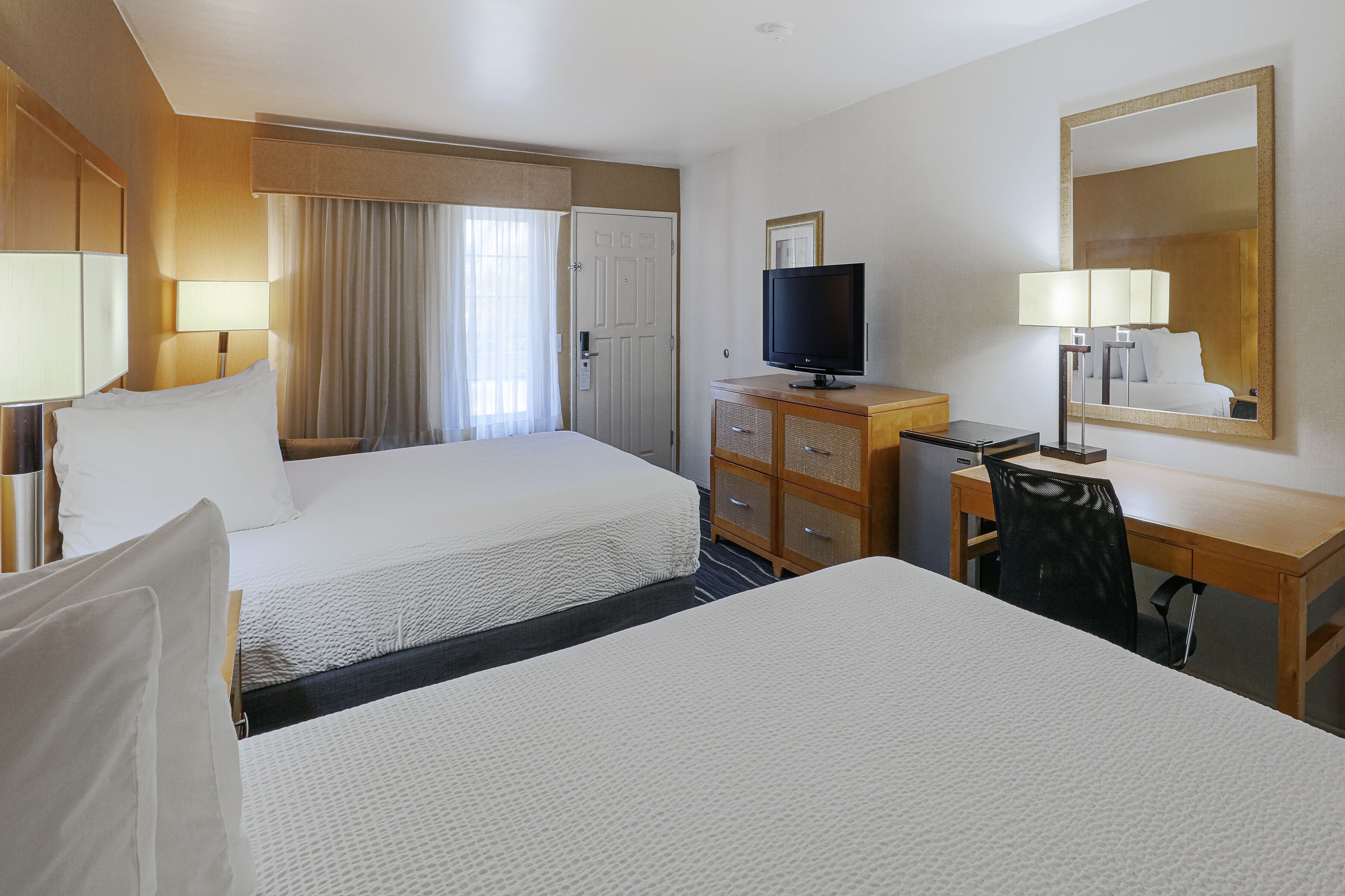 A hotel room with two beds, a television, a desk, and a mirror.