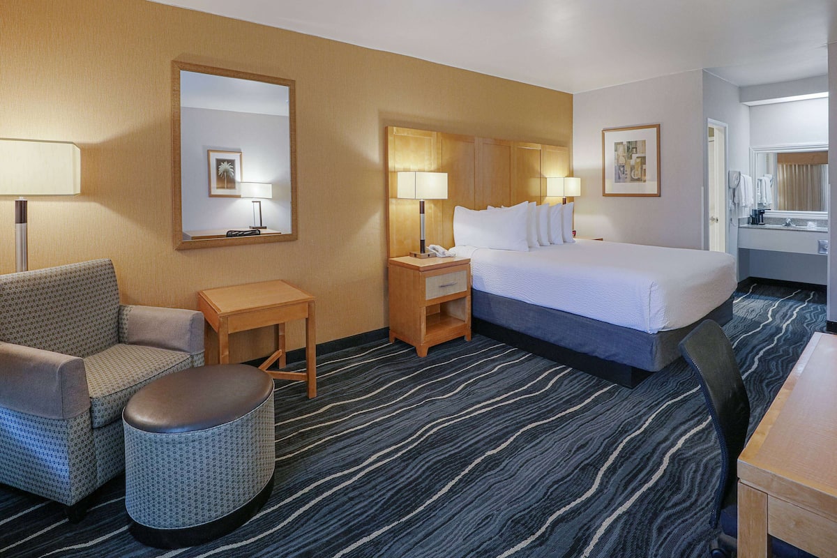 A hotel room with a bed, a desk, a chair, a small table, and a trash bin.