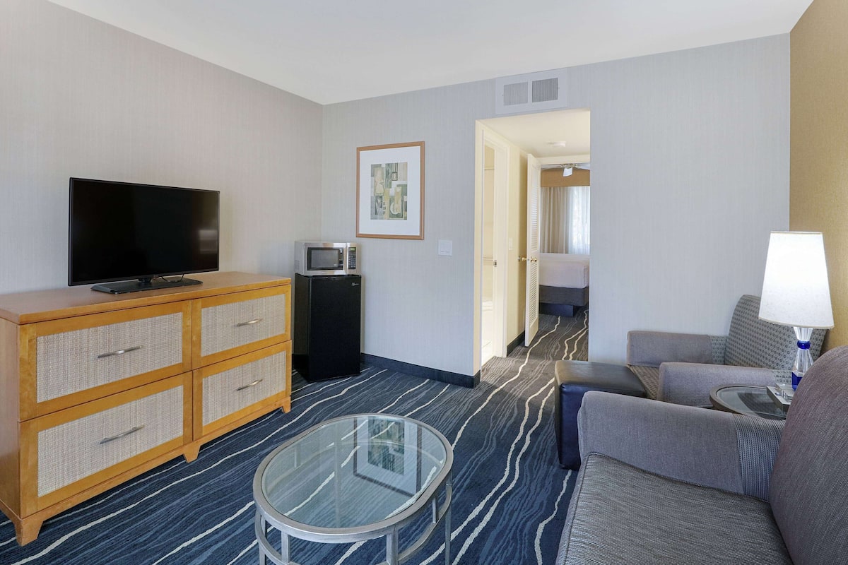 Ein Hotelzimmer mit Flachbildfernseher, Mikrowelle, Glastisch, Sofa und Lampe.