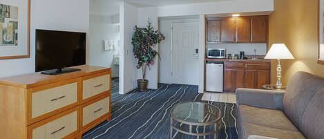 A living room with a television, a sofa, a coffee table, and a kitchen area with cabinets and appliances.