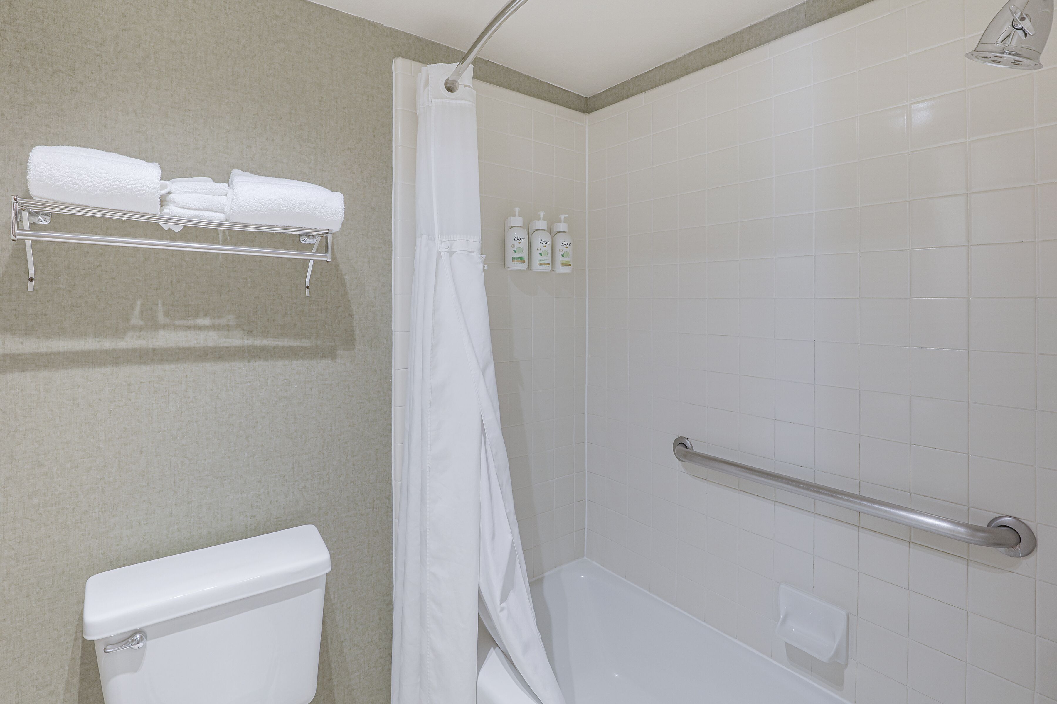 A bathroom with a toilet, a shower with a grab bar, and a towel rack with folded towels.