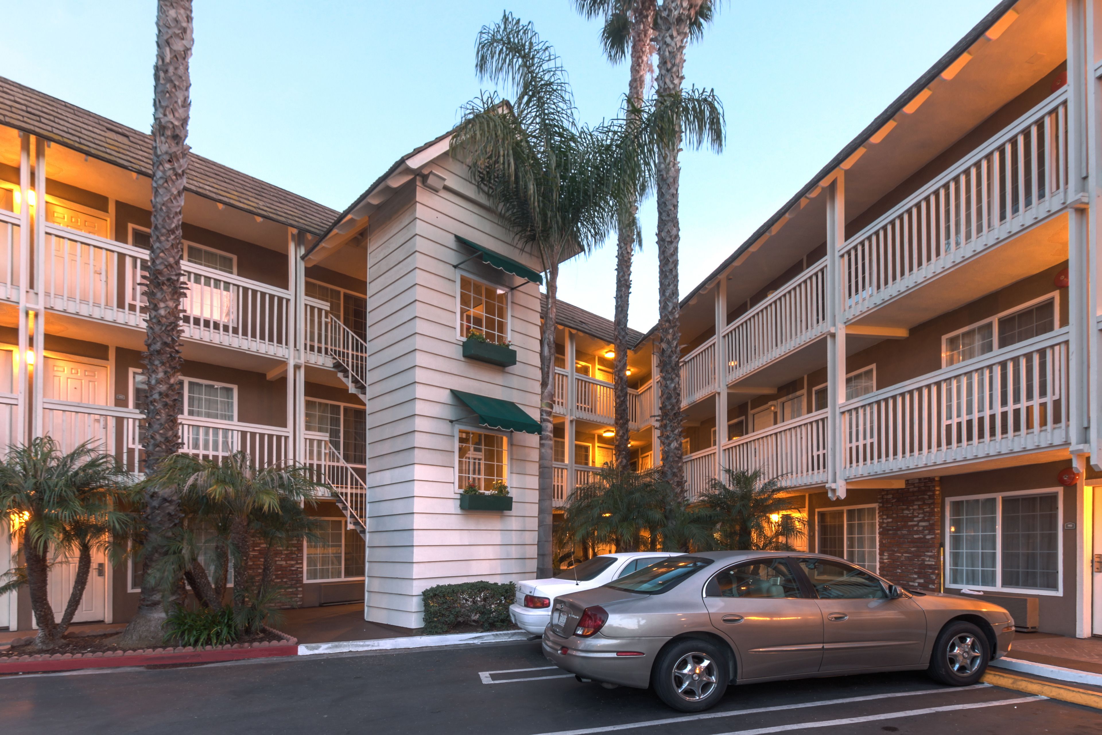 A multi-story hotel with balconies, palm trees, and a parking area.