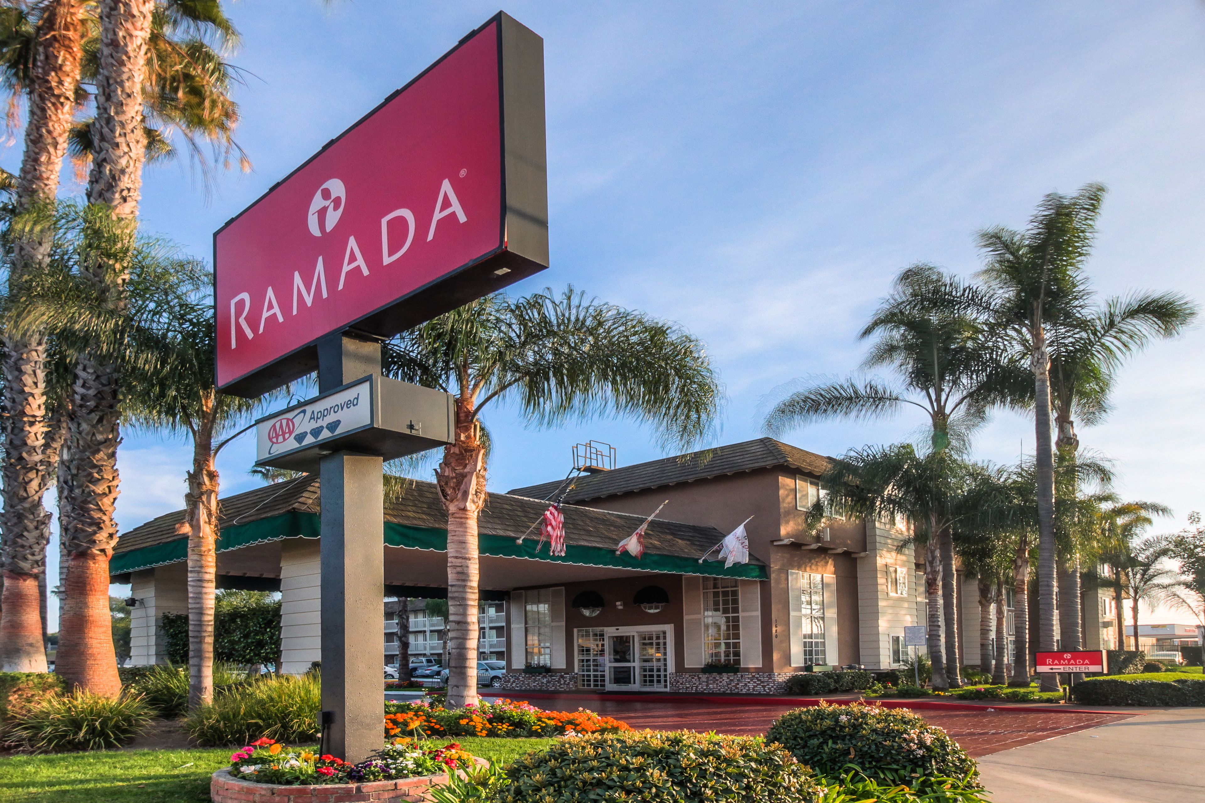 A Ramada hotel with a large sign, palm trees, and a well-maintained garden.