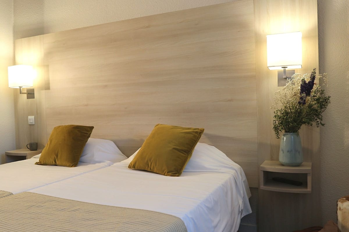 A hotel room with a large bed, two pillows, bedside lamps, and a vase with flowers.