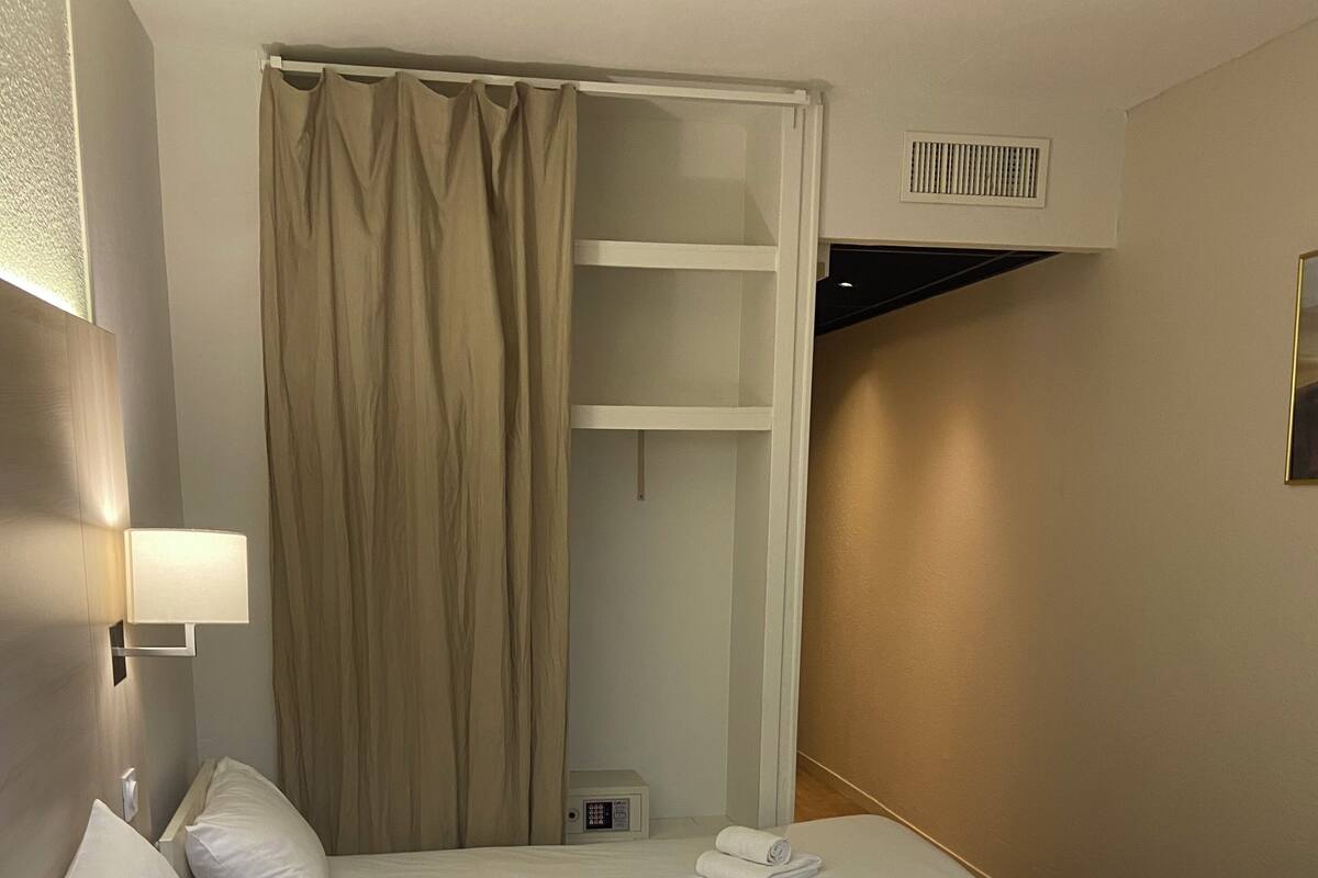 A hotel room with two beds, a wardrobe, a bedside lamp, and a thermostat.