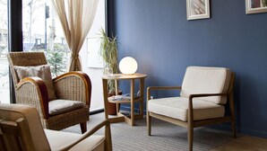 A room with a large window, two wicker chairs, a small table with a lamp, and framed pictures on the wall. - Hôtel d'Orsay  (Toulouse)
