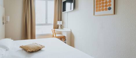 A hotel room with a bed, a desk, a chair, a TV, and a framed picture on the wall.