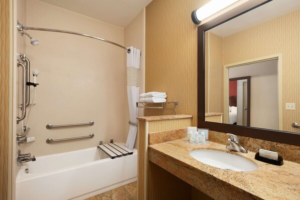 A bathroom with a bathtub, grab bars, a towel rack, a sink, and a mirror.