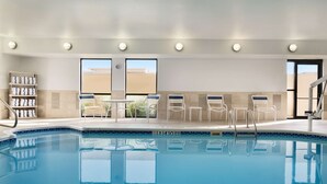 A swimming pool with lounge chairs and a sunbathing area, surrounded by a tiled wall and a wooden shelf with towels. - Hampton Inn Battle Creek (Battle Creek)
