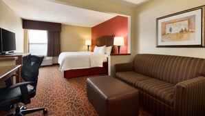 A hotel room with a bed, a sofa, a desk with a chair, and a television. - Hampton Inn Battle Creek (Battle Creek)