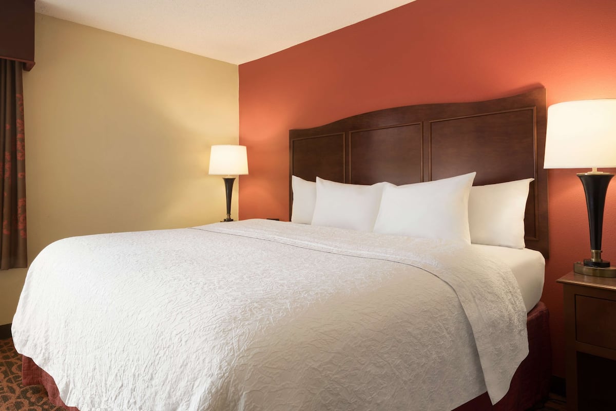 A neatly made bed with a white bedspread and pillows, a wooden headboard, and two bedside lamps on either side.