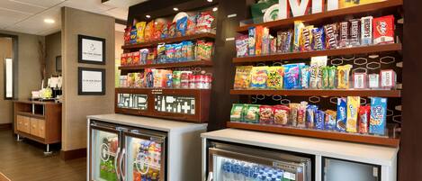 Zona de exhibición de aperitivos con diversos alimentos y bebidas envasadas, como papas fritas, galletas y bebidas embotelladas.