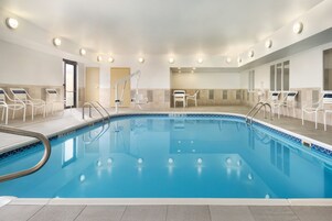 An indoor swimming pool with clear water, surrounded by white lounge chairs and a tiled floor.