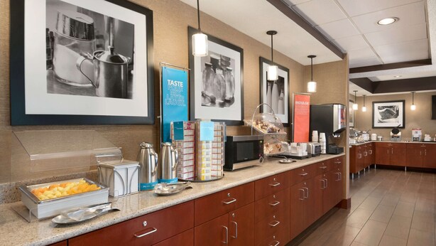 A modern kitchen with stainless steel appliances, a buffet setup, and framed pictures on the wall. - Hampton Inn Battle Creek (Battle Creek)