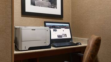 A desk with a printer and a laptop, a framed picture on the wall, and a chair.