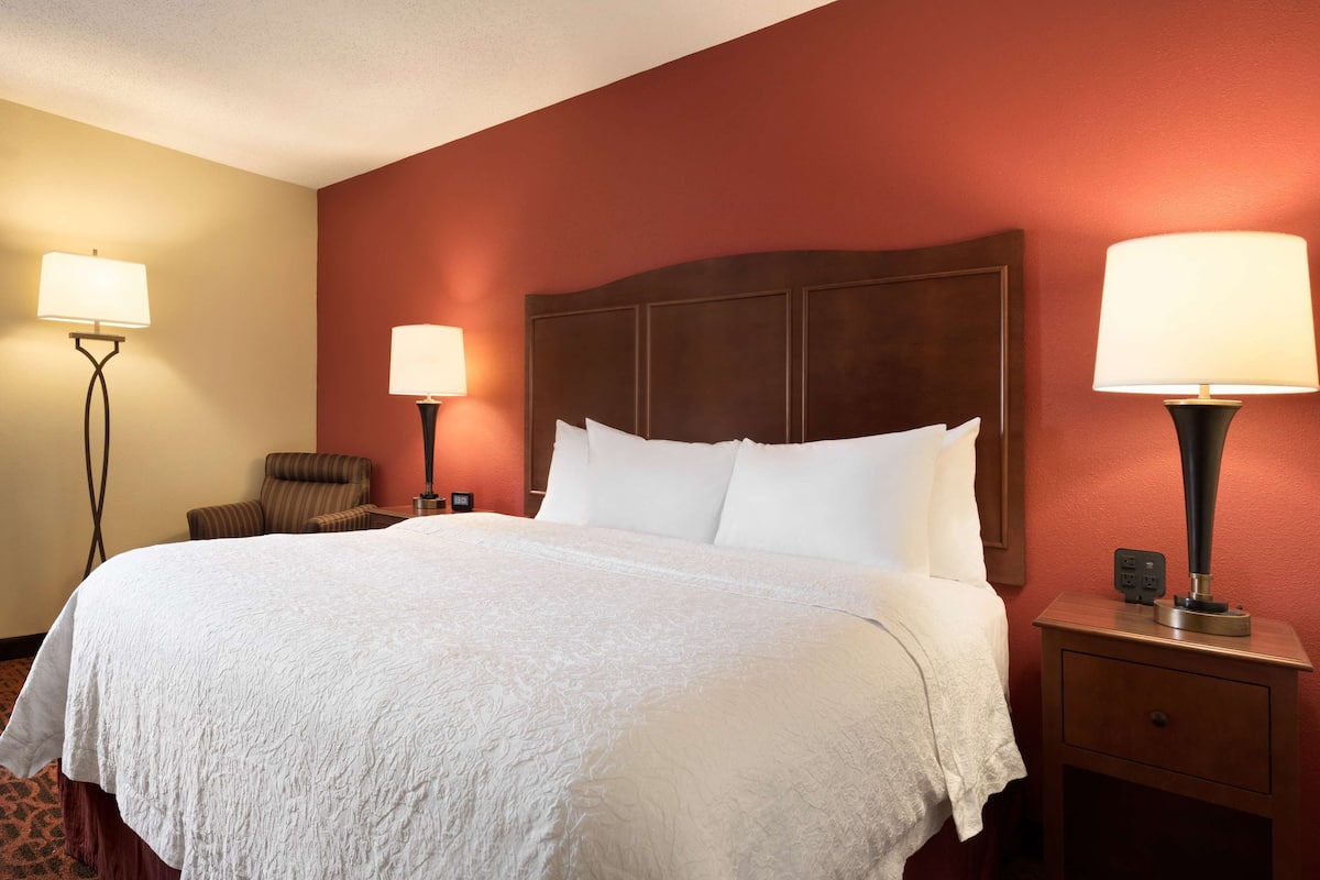 A hotel room with a large bed, two bedside lamps, a chair, and a nightstand with a lamp.