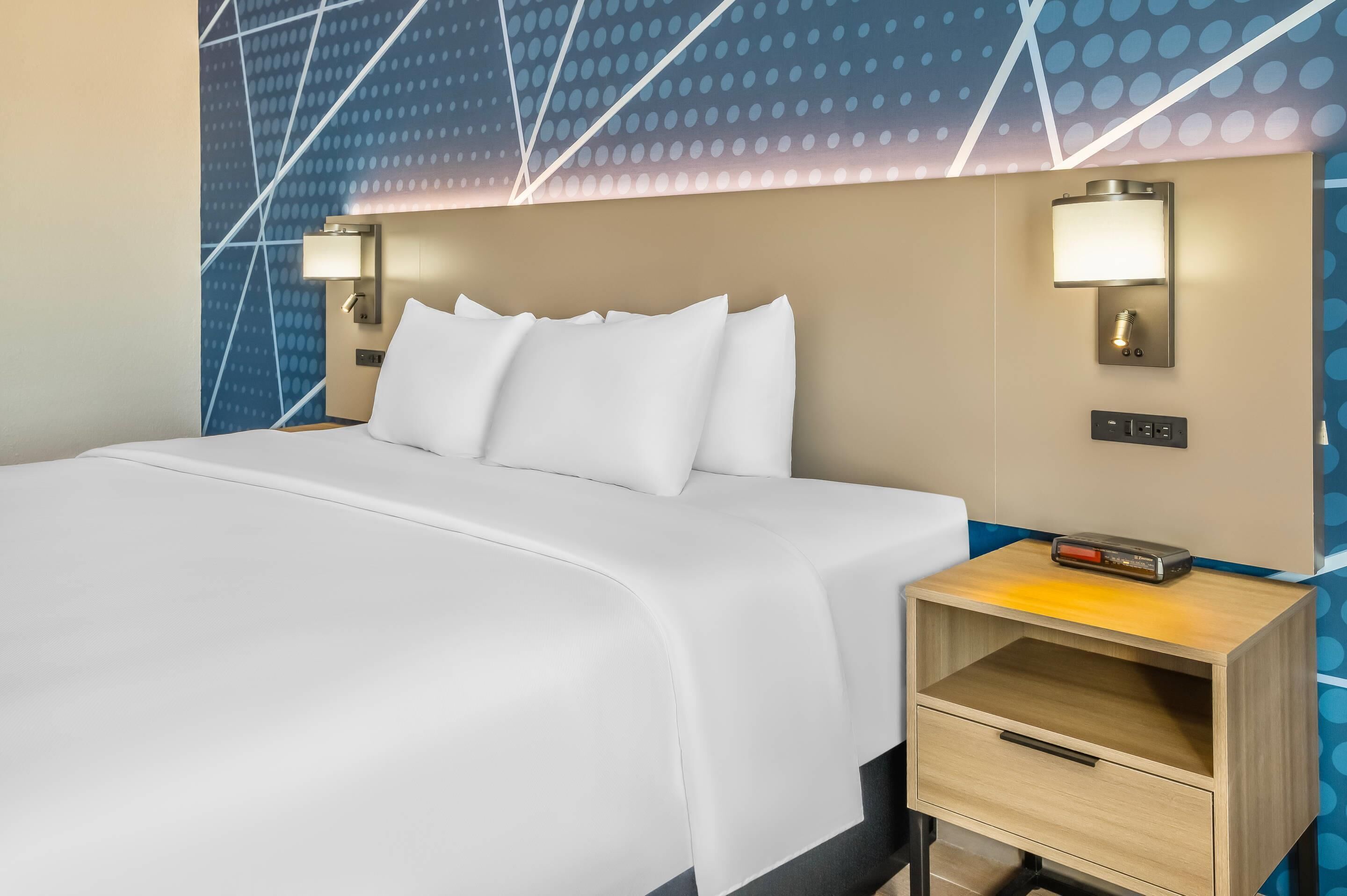 A hotel room with a neatly made bed, two wall-mounted nightstands, and a modern wall design.