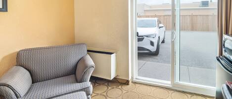 A living room with a sofa, a radiator, and a sliding glass door leading to a parking area with a white car.