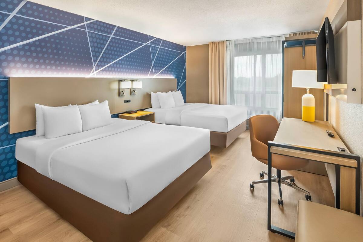 A hotel room with two beds, a desk, a chair, and a TV.