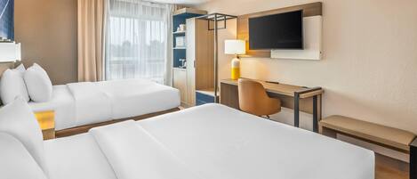 A hotel room with two beds, a desk, a chair, a TV, and a bookshelf.