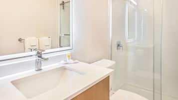 Un baño con lavamanos blanco, un espejo, cabina de ducha e inodoro.