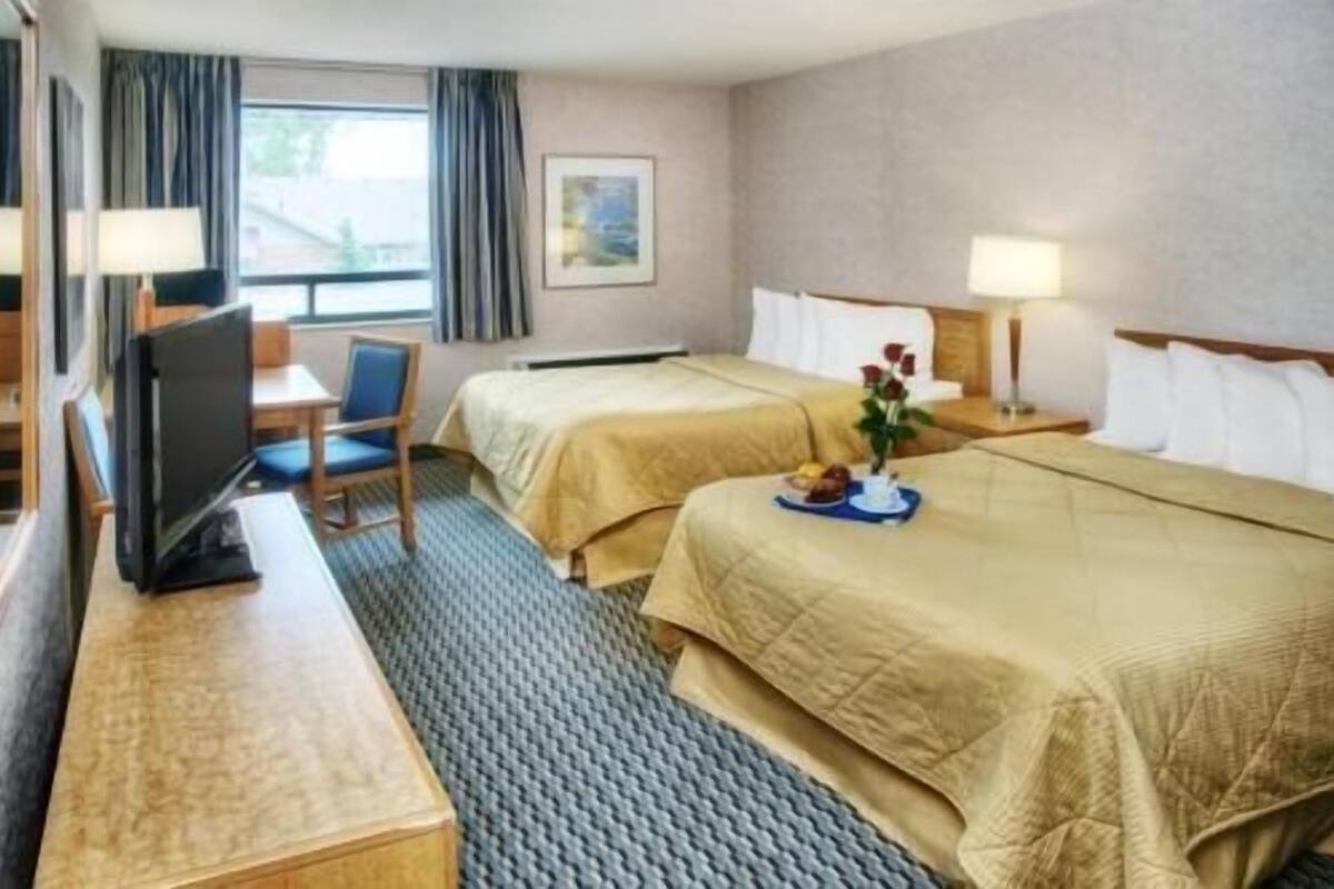 A hotel room with two beds, a desk, a chair, a TV, and a window with curtains.